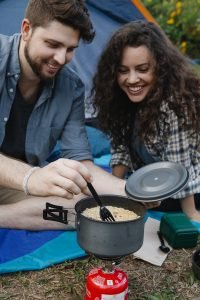 Hungry young couple cooking food on camping stove and smiling